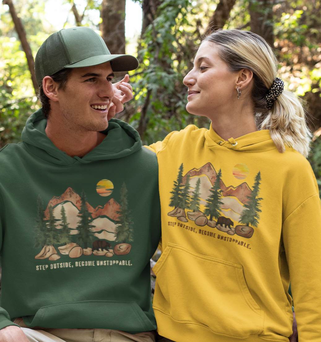 Couple wearing matching Mountain Bear Hoodies with a forest and bear design, featuring the inspiring phrase 'Step Outside, Become Unstoppable.