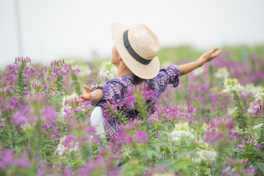 A young woman with loose hair and a light dress stands among lavender fields, arms extended toward the blue sky, embodying freedom and connection with nature. This serene scene evokes feelings of peace and happiness.