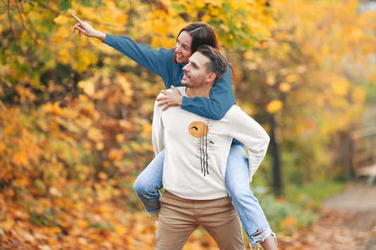 A man carries his partner on his back while walking through an autumn forest, surrounded by trees with warm-colored leaves like red, orange, and yellow, symbolizing love and fun in nature.